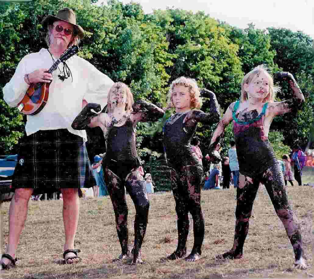 Magoo poses with three children who are coated in mud and flexing their muscles.